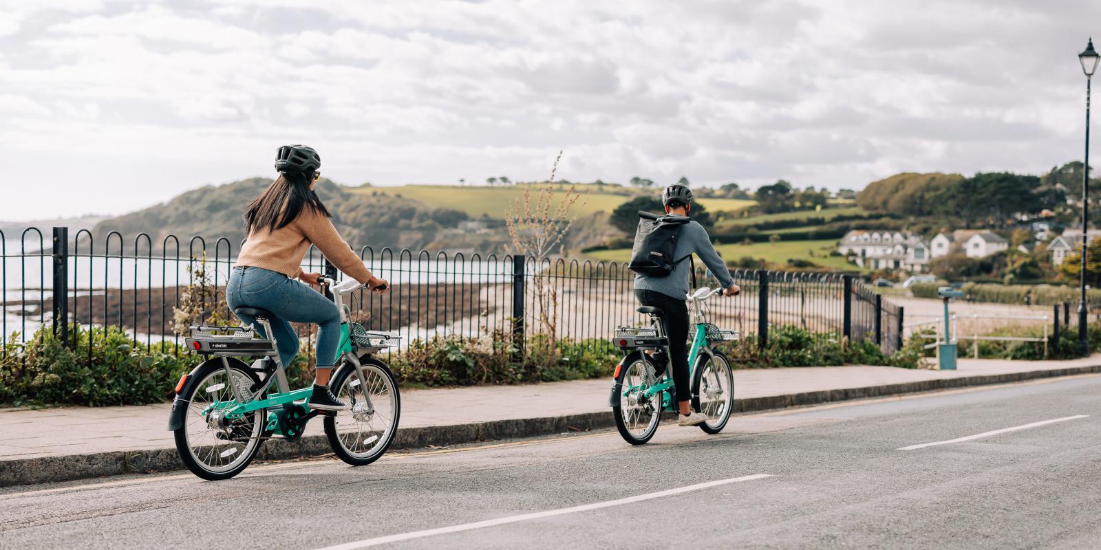Man and woman riding Beryl bikes along coast road in Cornwall