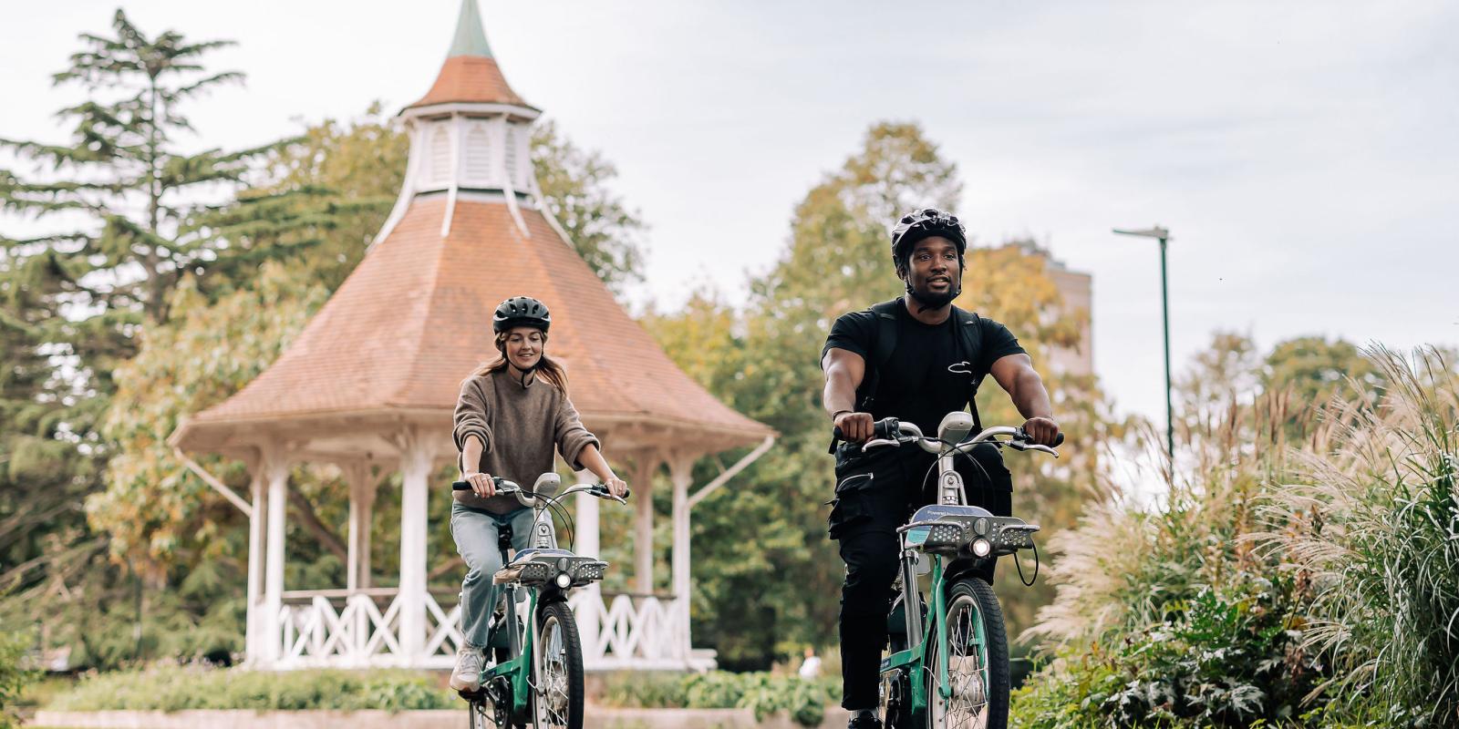 Two Beryl riders enjoying a bike journey in Norwich through a park  