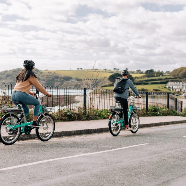 Man and woman riding Beryl bikes along coast road in Cornwall