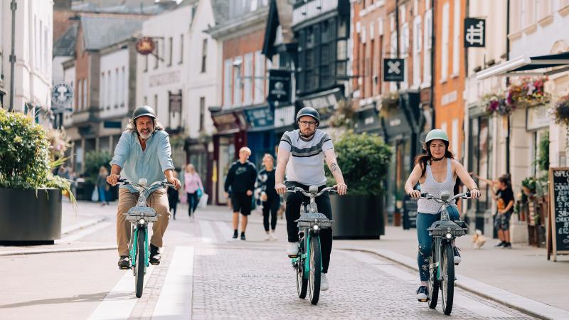 Two men and a woman riding Beryl bikes in a high street